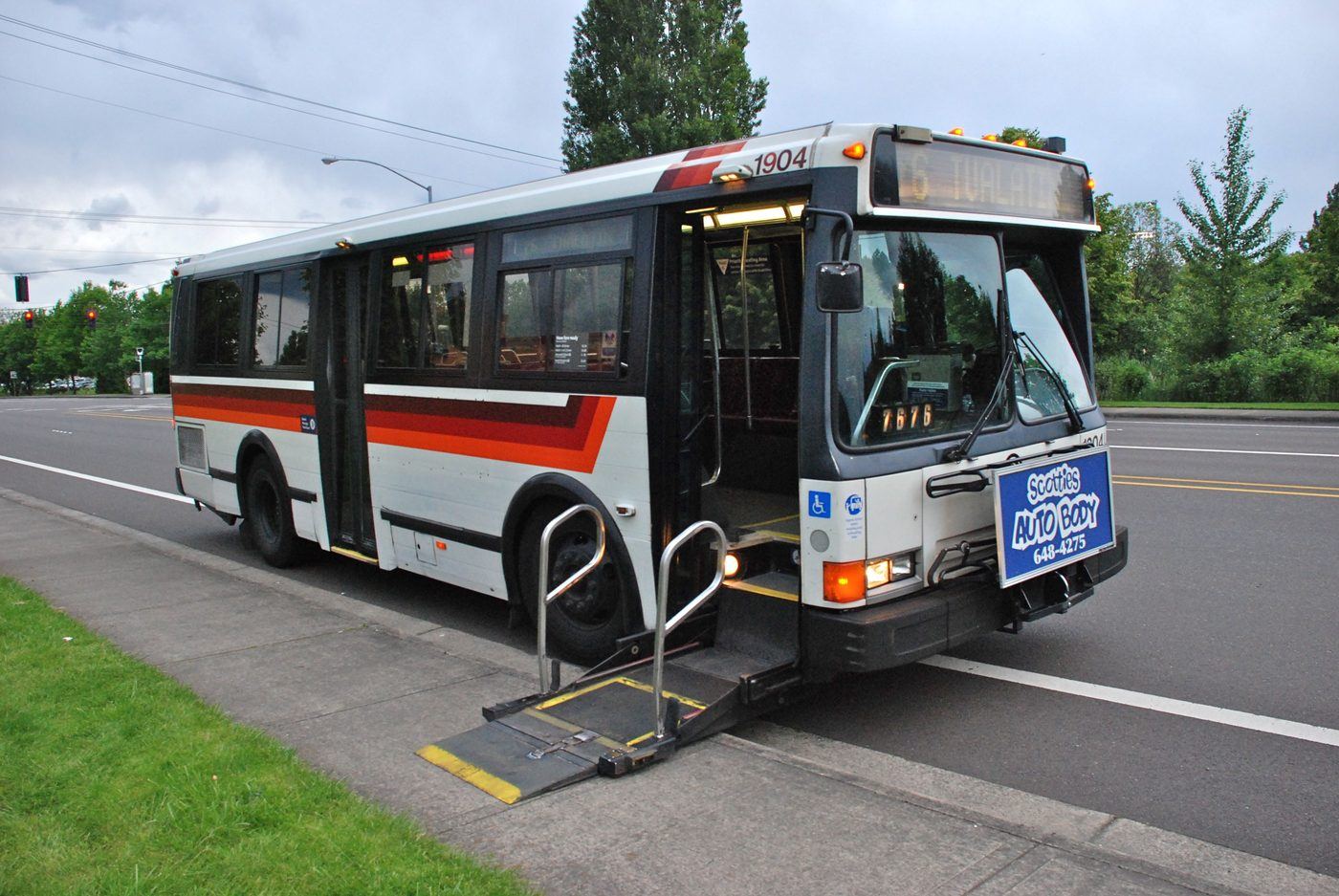 A public bus at the curb with its front-door wheelchair lift fully extended down to the sidewalk.