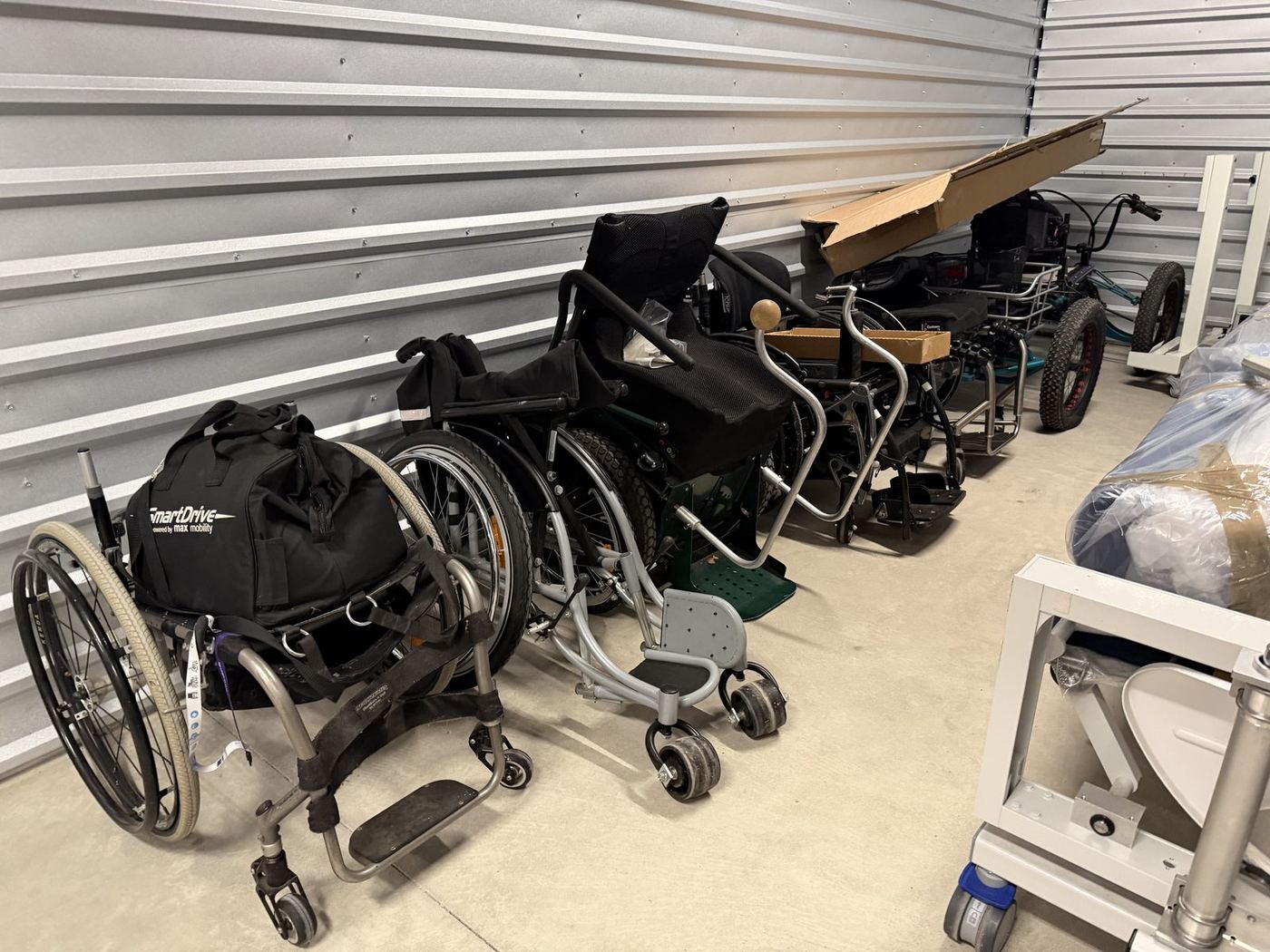 Wheelchairs, a SmartDrive bag, and a rugged trike in Everyday Abilities Equipment Library storage.