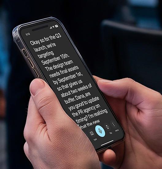 Two hands holding a phone that shows live captions of a conversation as large white text on a dark screen.