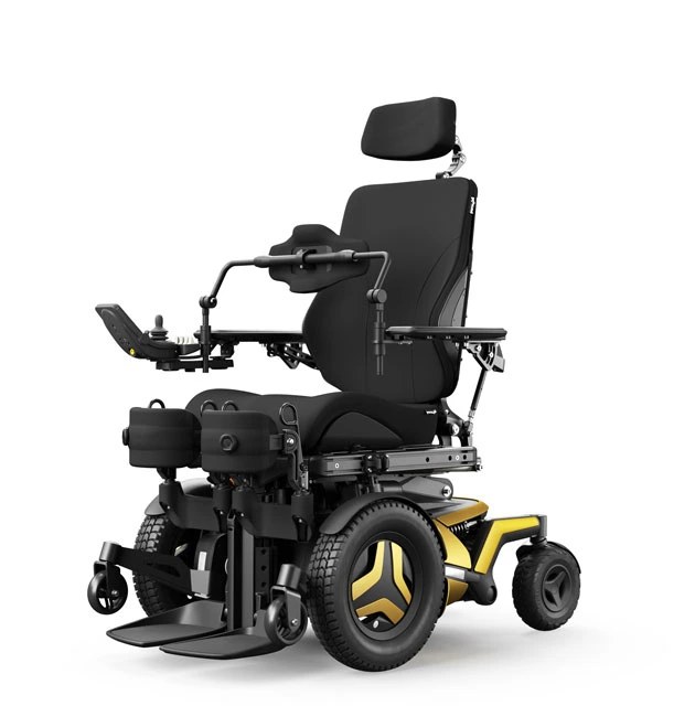 Permobil F5 Corpus VS standing power wheelchair: an empty front-wheel-drive chair with chest and knee supports, articulating footplates, and gold-accented base, shown against a white background.
