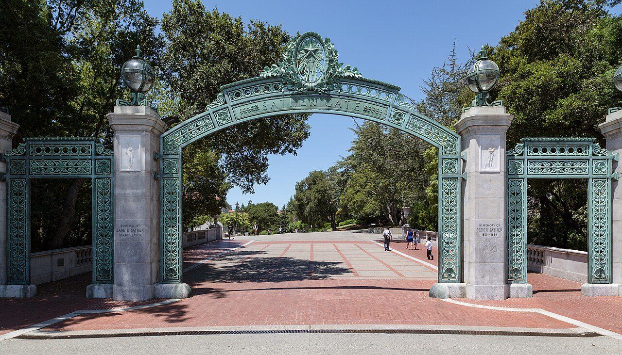 Sather Gate at UC Berkeley, bronze and granite archway opening onto a tree-lined walk toward Sproul Plaza.