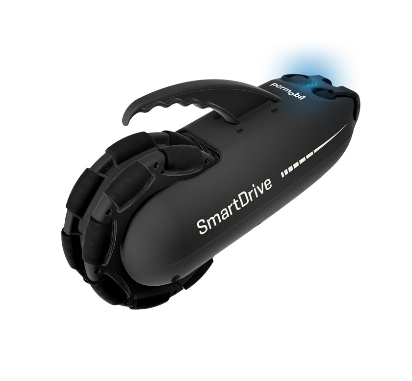 Permobil SmartDrive MX2+ power assist unit: a black under-chair drive with an OmniWheel, top carry handle, and SmartDrive branding, shown empty against a white background.