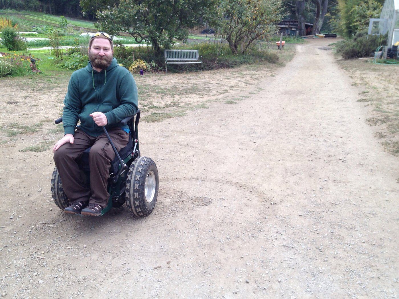 Walter Delson, founder of Everyday Abilities, in an all-terrain power wheelchair on a path beside a community garden.